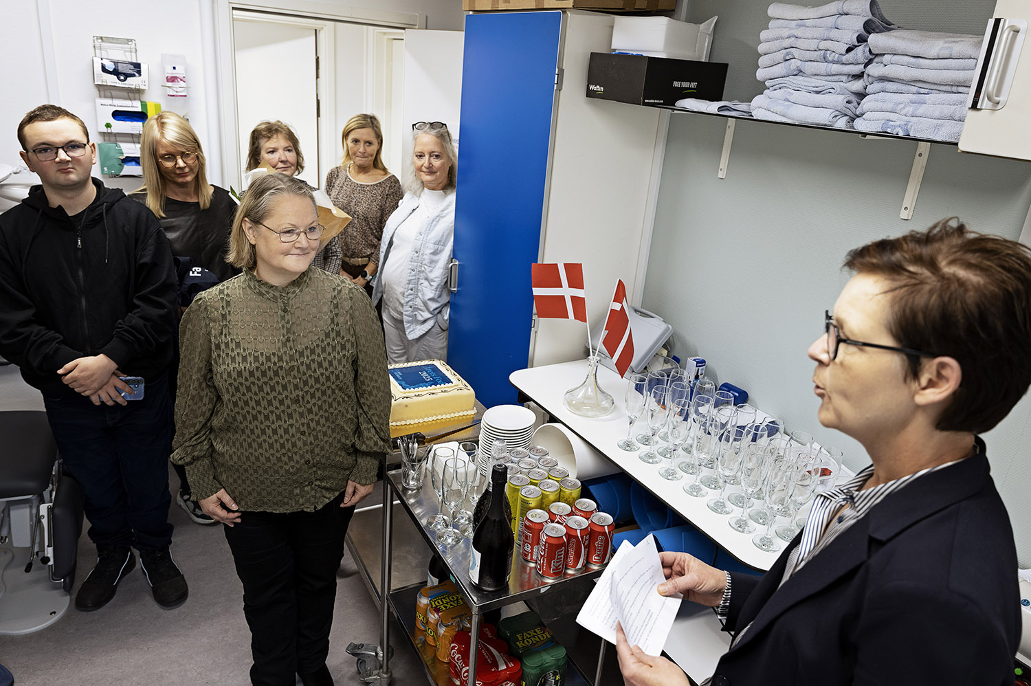 Cille Holse holder tale for Dorte Vilhelmsen, mens gæsterne lytter i baggrunden. På borde står champagneglas, boblevand, sodavand og kage klar.