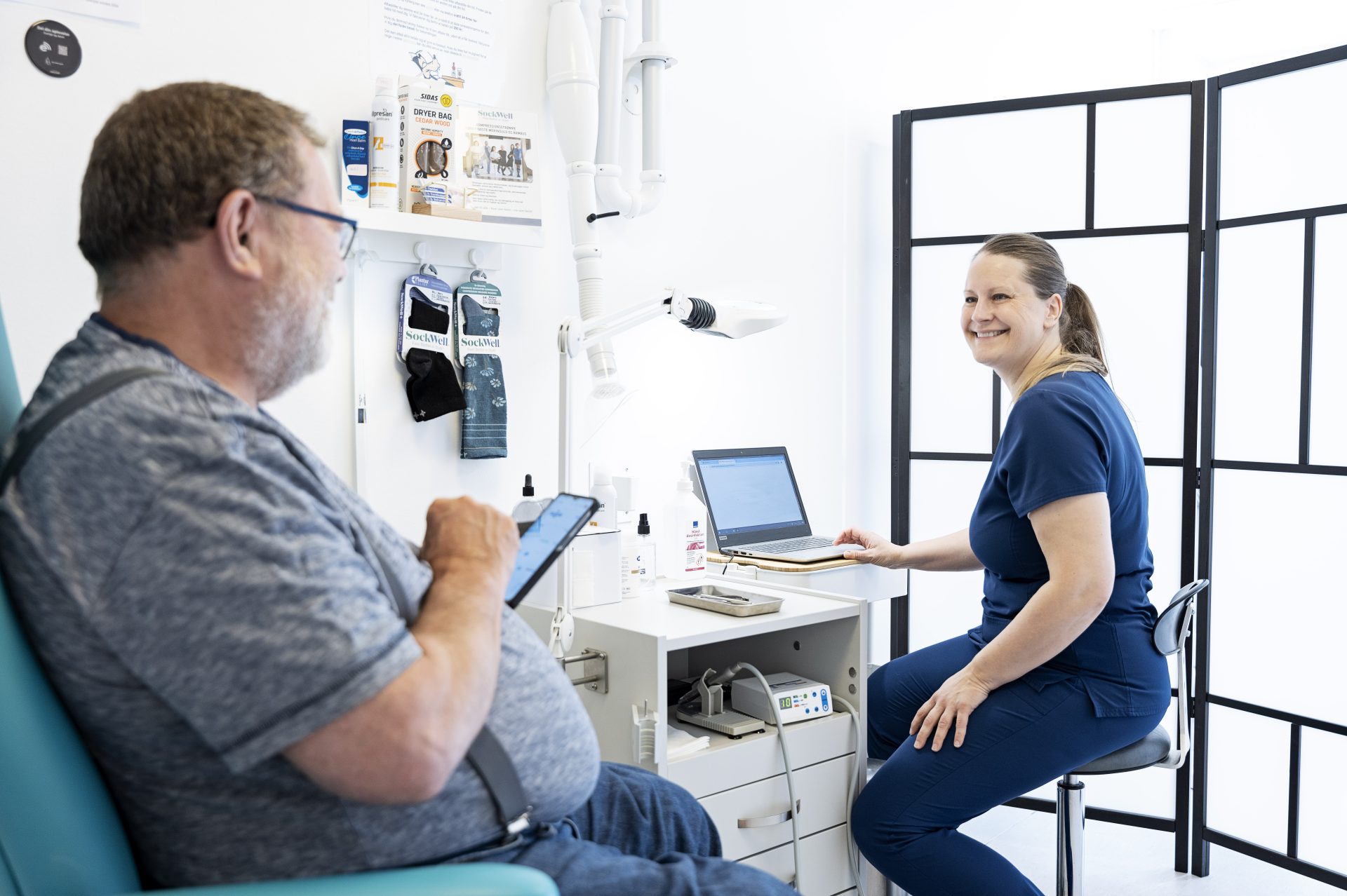 Patient sidder med telefon i hånden overfor fodterapeut. De er ved at finde en ny tid.